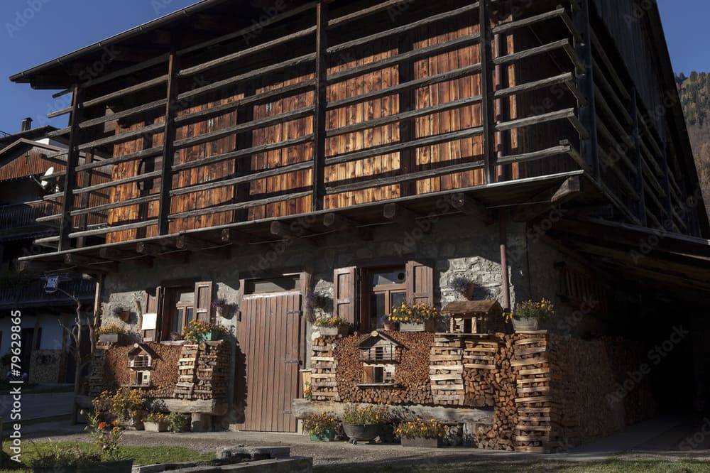 Tradizionale casa di legno a Sauris con legna da ardere e decorazioni floreali